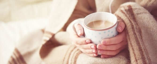 Woman in a blanket sitting with a hot cup of coffee